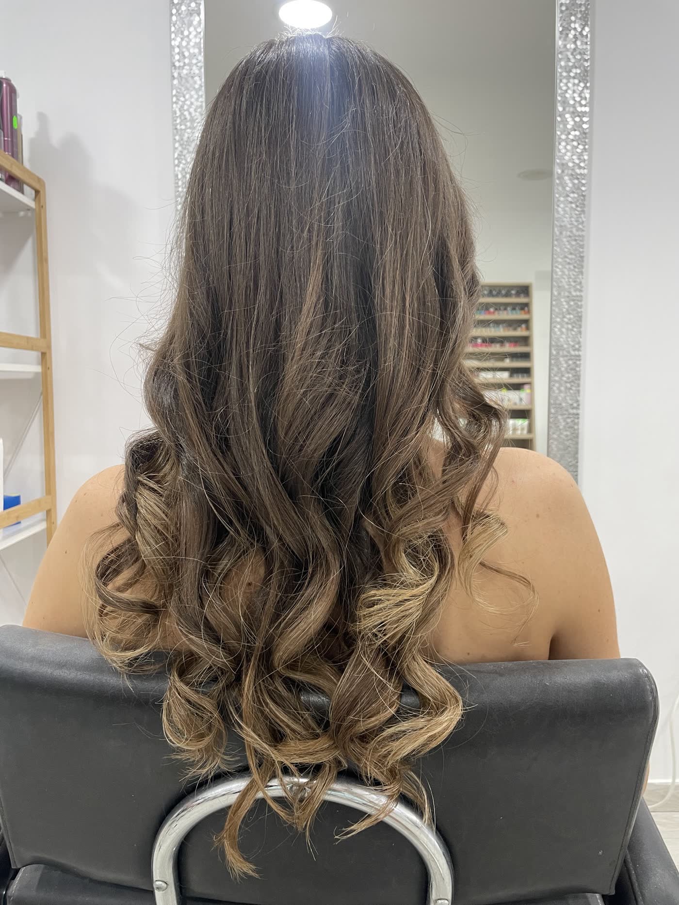Bucle lungi, balayage în nuanțe de ciocolată și caramel, clienta în scaunul de coafor al salonului